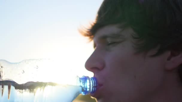 facet pije wodę z butelki o zachodzie słońca - Materiał filmowy, wideo