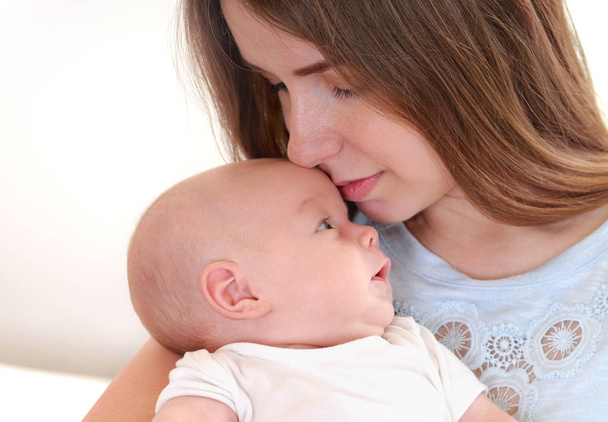 Молода мати тримає свою новонароджену дитину і цілує його
 - Фото, зображення