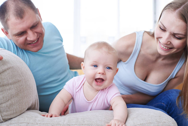 Joyful child crawling on sofa and happy parents looking at it - Foto, immagini