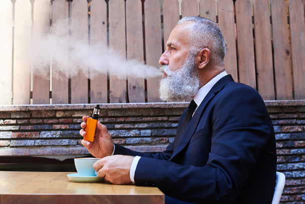 Όμορφος κύριος κάπνισμα electrocigarette πάνω από ένα φλιτζάνι καφέ - Φωτογραφία, εικόνα