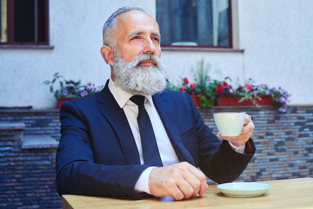 Bearded male drinking coffee while sitting - Фото, изображение