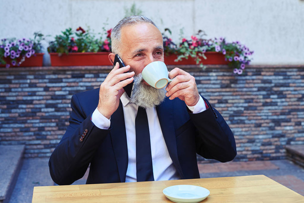 Улыбающийся джентльмен разговаривает по телефону, когда пьет кофе
 - Фото, изображение