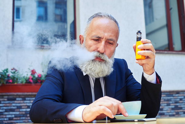 Homme expirant fumée tout en surfant au téléphone sur une tasse de café
 - Photo, image