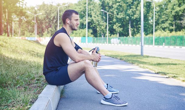 Serious athlete sitting on curb - Zdjęcie, obraz