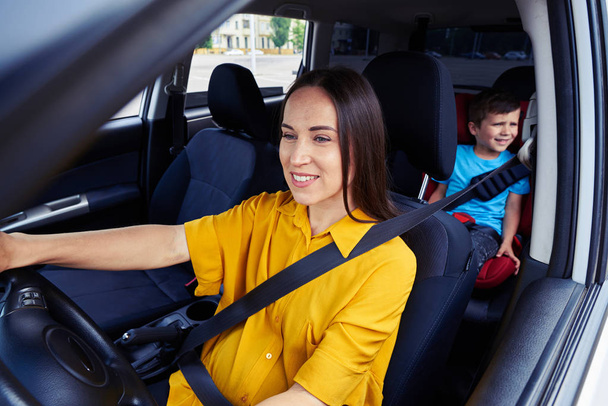 Mujer conduciendo un coche, niño detrás
 - Foto, imagen