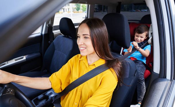 Hezká žena řidičské auto s syn sedí v dětské autosedačky - Fotografie, Obrázek