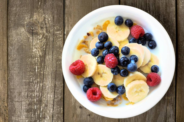 Breakfast cereal with blueberries, bananas and raspberries on wood - Photo, Image
