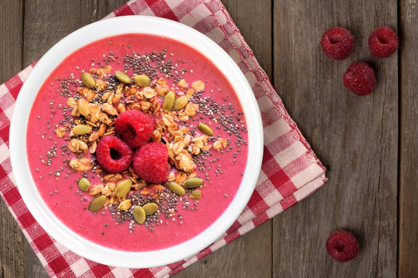Smoothie bowl with raspberries, granola and chia seeds on a rustic wood background with checkered cloth, overhead view - Photo, Image