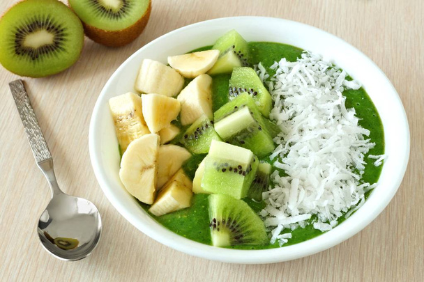 Green smoothie bowl with bananas, fresh kiwi and coconut table scene - Photo, Image