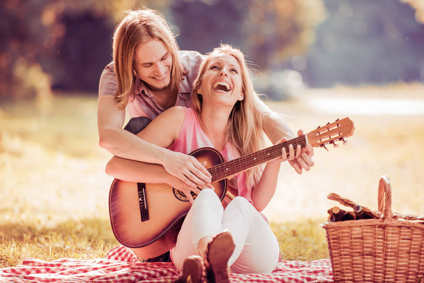 Мужчина играет на гитаре с девушкой на пикнике
 - Фото, изображение
