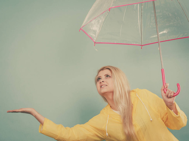Woman wearing raincoat holding umbrella checking weather - Zdjęcie, obraz