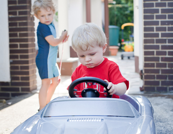 Dois irmãos pequenos crianças brincando com o carro de brinquedo grande
 - Foto, Imagem