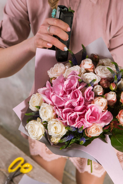 Florist wrapping bouquet of rose flowers. - Фото, изображение