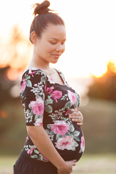 Femme enceinte tenant son estomac à l'extérieur pendant un coucher de soleil
 - Photo, image