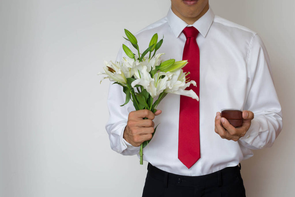 Young man in a suit proposing with an engagement ring and lilies - Foto, Bild
