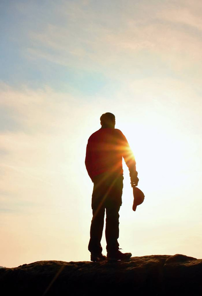 Wanderer in rotem Sweatshirt mit roter Mütze auf felsigem Gipfel. Mann wacht über Tal zur Sonne. schöner Moment das Wunder der Natur.  - Foto, Bild