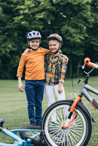 дети в шлемах стоят рядом с велосипедами в парке
 - Фото, изображение