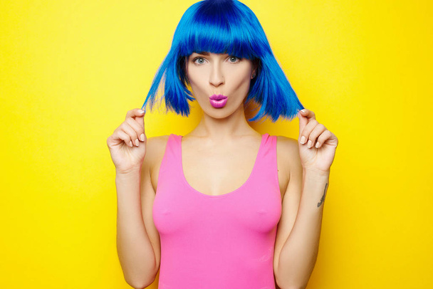 Kaunis nuori seksikäs tyttö sininen peruukki ja vaaleanpunainen uimapuku on hauskaa ja pelleillä keltaisella taustalla
 - Valokuva, kuva
