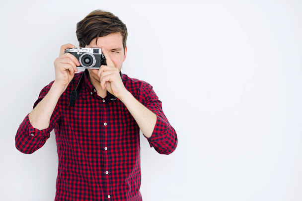 Young guy stands at a white wall and photographed on a mirrorless camera - Photo, Image