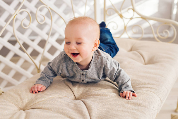 Adorable laughing baby boy in sunny bedroom. Newborn child relaxing. Nursery for young children.Family morning at home. Little kid lying on tummy - Photo, Image