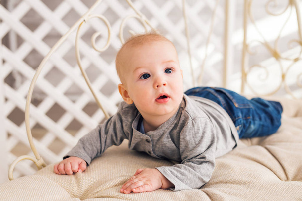 Αξιολάτρευτο μωρό αγόρι στην ηλιόλουστη κρεβατοκάμαρα. Νεογέννητο παιδί χαλαρωτικό. Φυτώριο για μικρά παιδιά. Οικογένεια το πρωί στο σπίτι. Μικρό παιδί ξαπλωμένη μπρούμυτα - Φωτογραφία, εικόνα