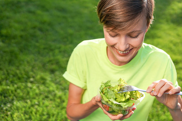 Портрет привлекательной белой улыбающейся женщины, кушающей салат
 - Фото, изображение