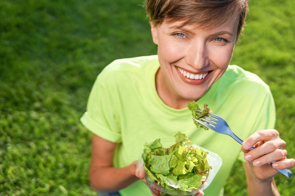 Портрет привлекательной белой улыбающейся женщины, кушающей салат
 - Фото, изображение