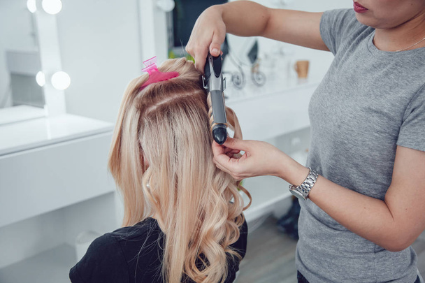 Hair stylist makes a curls for a girl, using hair styling. Hairdresser at work. - Zdjęcie, obraz