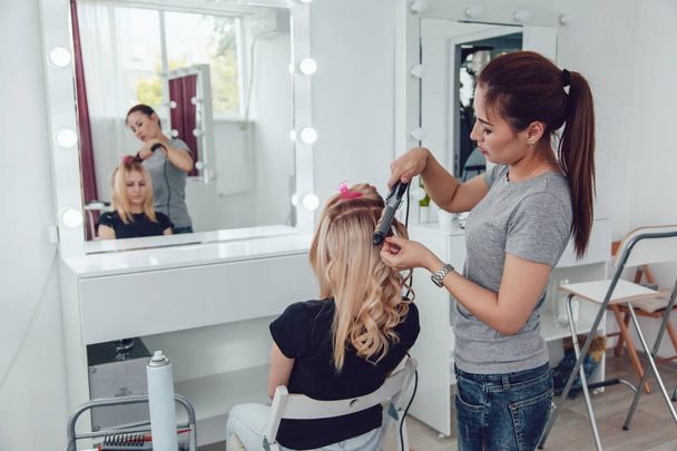 Hair stylist makes a curls for a girl, using hair styling. Hairdresser at work. - Φωτογραφία, εικόνα