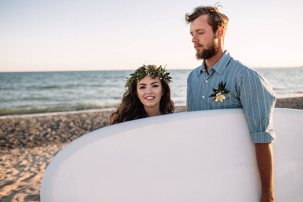 Happy surfers couple standing with surfboards on the sandy beach - 写真・画像
