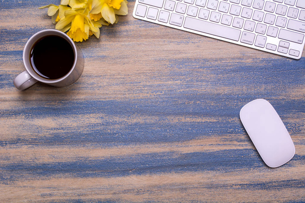 Posto di lavoro in ufficio con tastiera, narcisi, tazza di tè e mouse su uno sfondo di legno
. - Foto, immagini