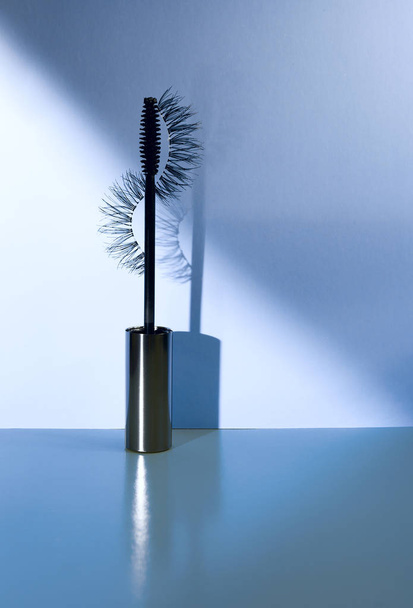 Applicator mascara and false eyelashes with drop shadow on blue background. - Photo, Image