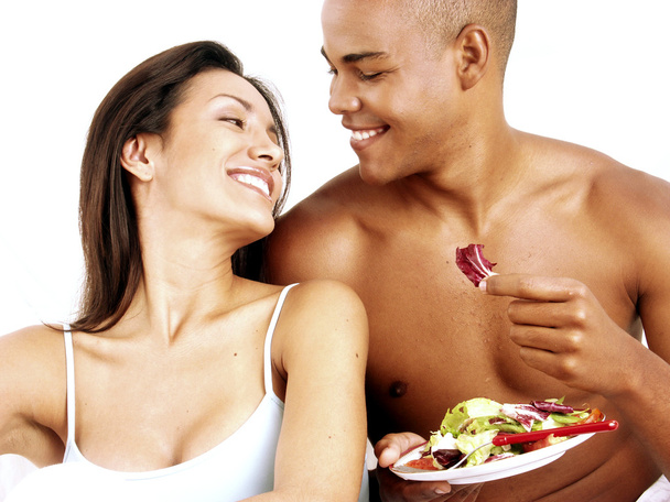 Young hispanic couple enjoying and eating vegetable salad on white background. - Фото, изображение