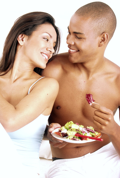 Young hispanic couple enjoying and eating vegetable salad on white background. - Foto, Imagen