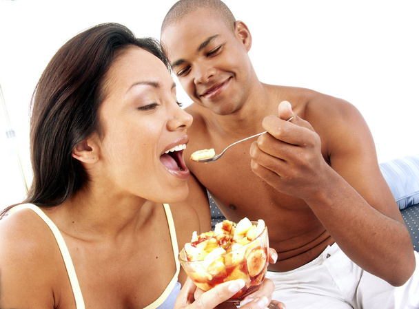 Young hispanic couple enjoying and eating fruit salad on bed. - Фото, изображение