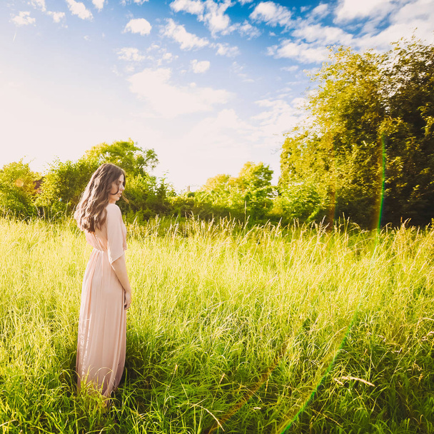 beautiful attractive lady of a young slender brunette girl with long dress walking through a green park with flowers at sunset lifestyle - Photo, image