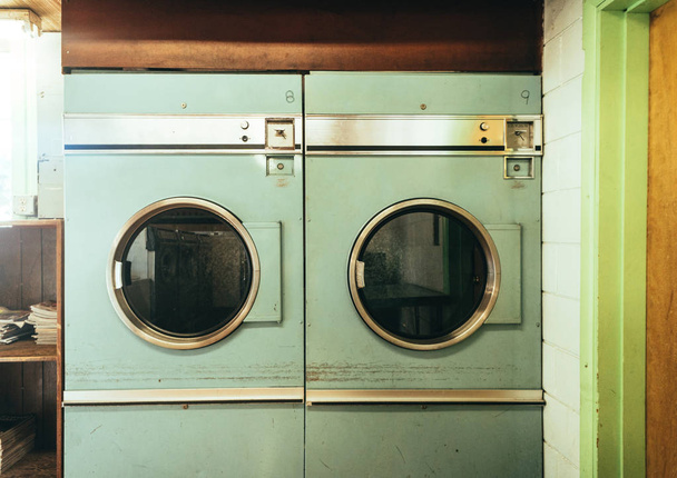 Старые избитые винтажные стиральные машины сидят в забегающей прачечной коврик показывает годы использования
.  - Фото, изображение