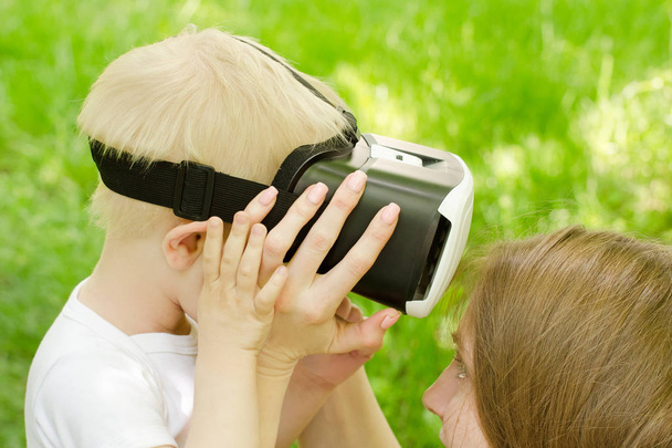 Mamma corregge suo figlio occhiali di realtà virtuale sullo sfondo di erba verde
 - Foto, immagini