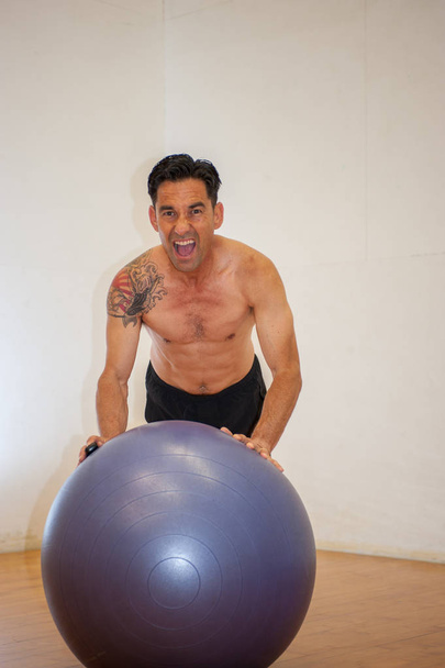 Hemdloser Mann trainiert auf Balanceball. - Foto, Bild