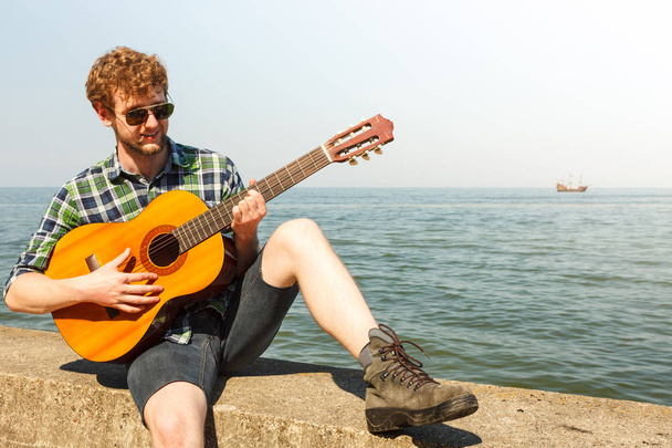 Young man hipster playing guitar by sea ocean. - Φωτογραφία, εικόνα