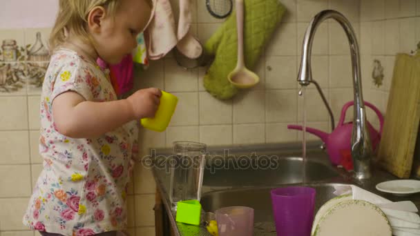 Little baby girl playing washing dishes - Footage, Video