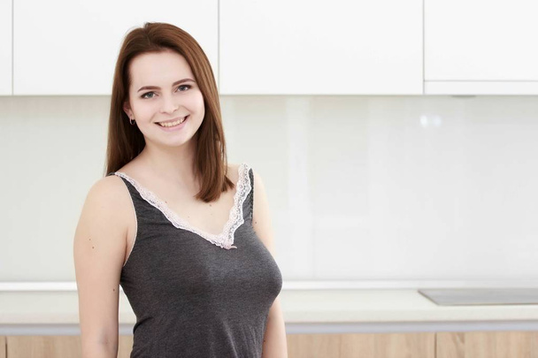 Serious attitude. Young smiling lady standing in a kitchen. - Zdjęcie, obraz