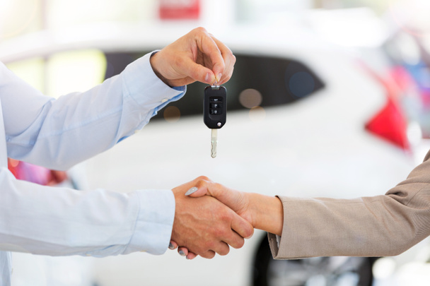 Car salesman handing car keys to woman in showroom - Foto, afbeelding