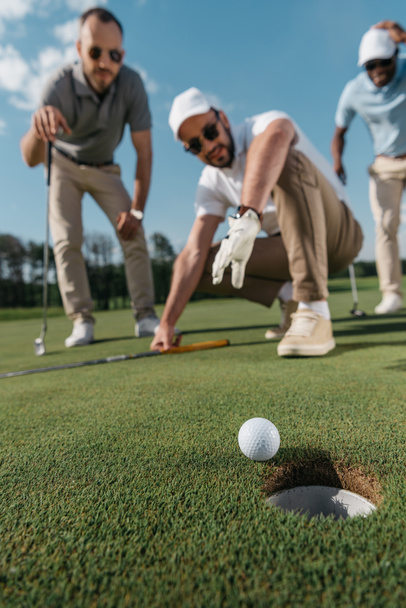 игроки в гольф смотрят на мяч возле лунки
 - Фото, изображение