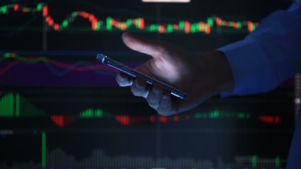 Ręka osoby z telefonu, wpisując tekst wiadomości na smartfonie, na tle ekranu Lcd z wykresu, wymiany rynku finansowego - wykres. - Materiał filmowy, wideo