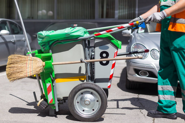 Εργαζόμενος από την εταιρεία καθαρισμού σε πράσινη στολή με κάδο απορριμμάτων. - Φωτογραφία, εικόνα