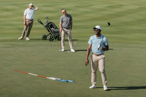 desportistas de pé com tacos de golfe em campo
 - Foto, Imagem