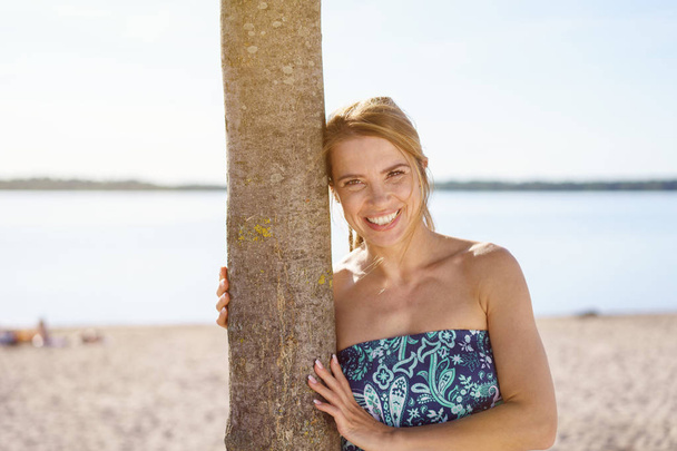Friendly relaxed young woman leaning on tree - Foto, afbeelding