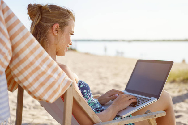 Young woman typing on laptop on beach - 写真・画像