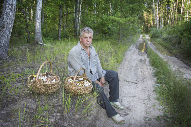 Kesällä mies, jolla on kaksi koria sieniä, istuu
 - Valokuva, kuva